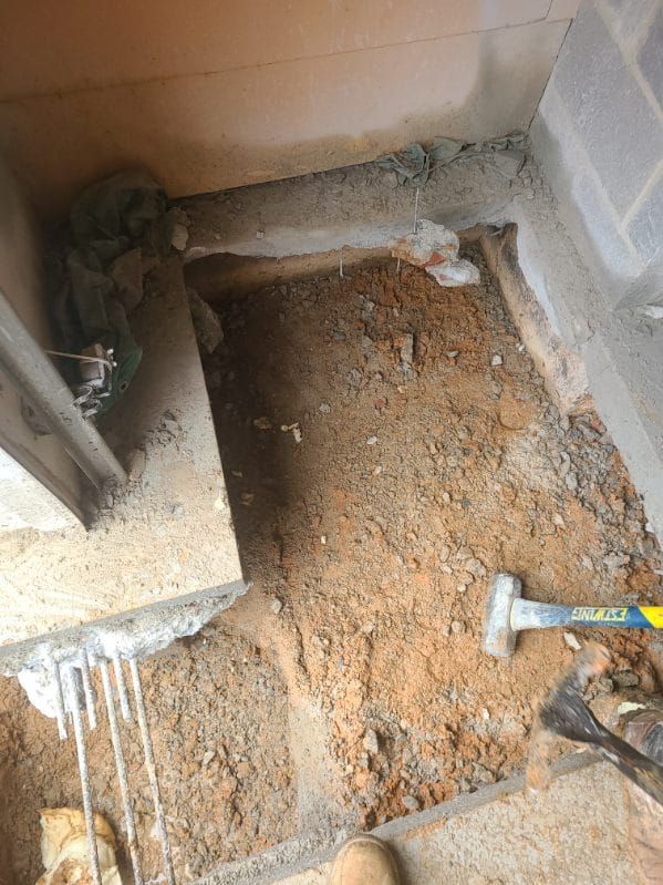 Excavated area in construction setting, dirt floor, concrete edges, a hammer and chisel present.