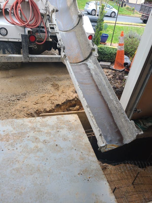 Concrete being poured from a truck's chute into a prepared form for a sidewalk or foundation.