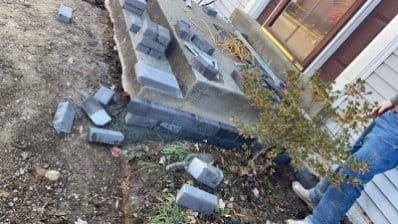 Damaged brick patio near a house with a person, bricks scattered on the ground.