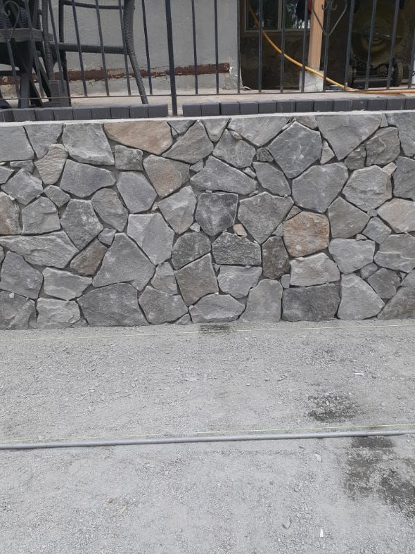 Stone wall with gray and tan rocks, built on a gravel surface.