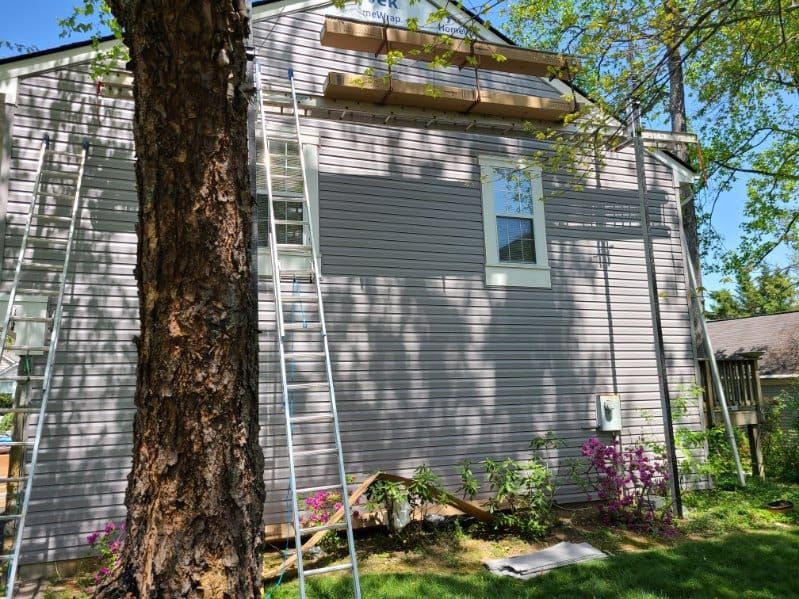 House exterior under renovation with ladders, grey siding, and wooden supports.
