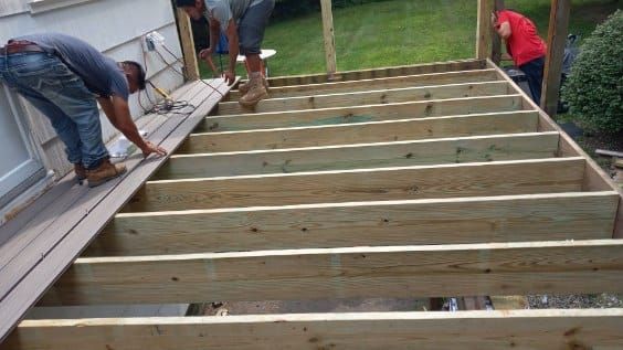 Men building a deck; installing composite planks over wooden joists; outdoors.