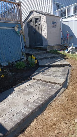 Stone pathway with steps leading to a shed next to a deck and building.