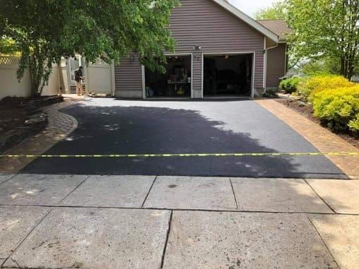 Newly paved asphalt driveway in front of a garage; a worker in the background.