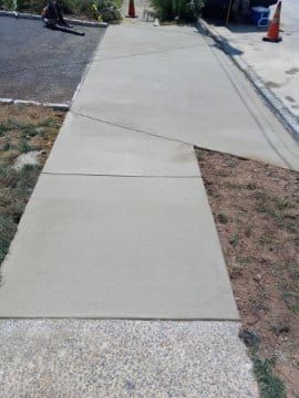 New concrete sidewalk next to parking lot; one section diagonal. Orange cones.