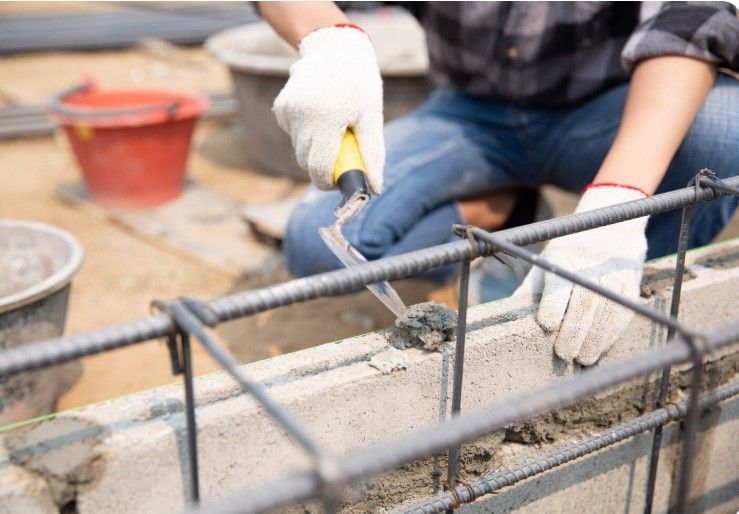 Person in gloves using a trowel to apply mortar to concrete blocks with rebar framing.