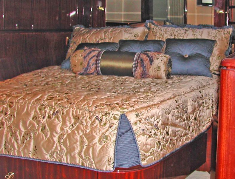 Bed with gold quilted bedding, navy blue pillows, and decorative bolsters on a wooden frame.