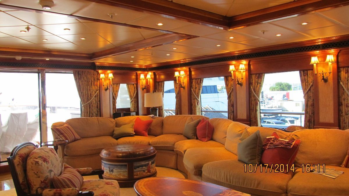 Luxurious yacht interior with large yellow sectional sofa and windows.