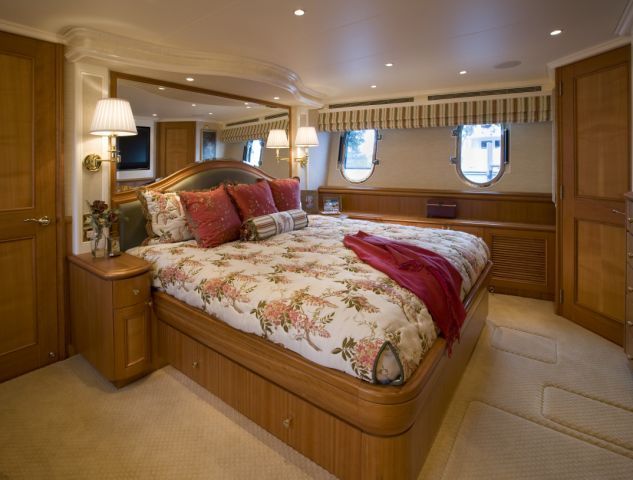 Bedroom on a yacht, with a large floral bed, wooden furniture, and porthole windows.