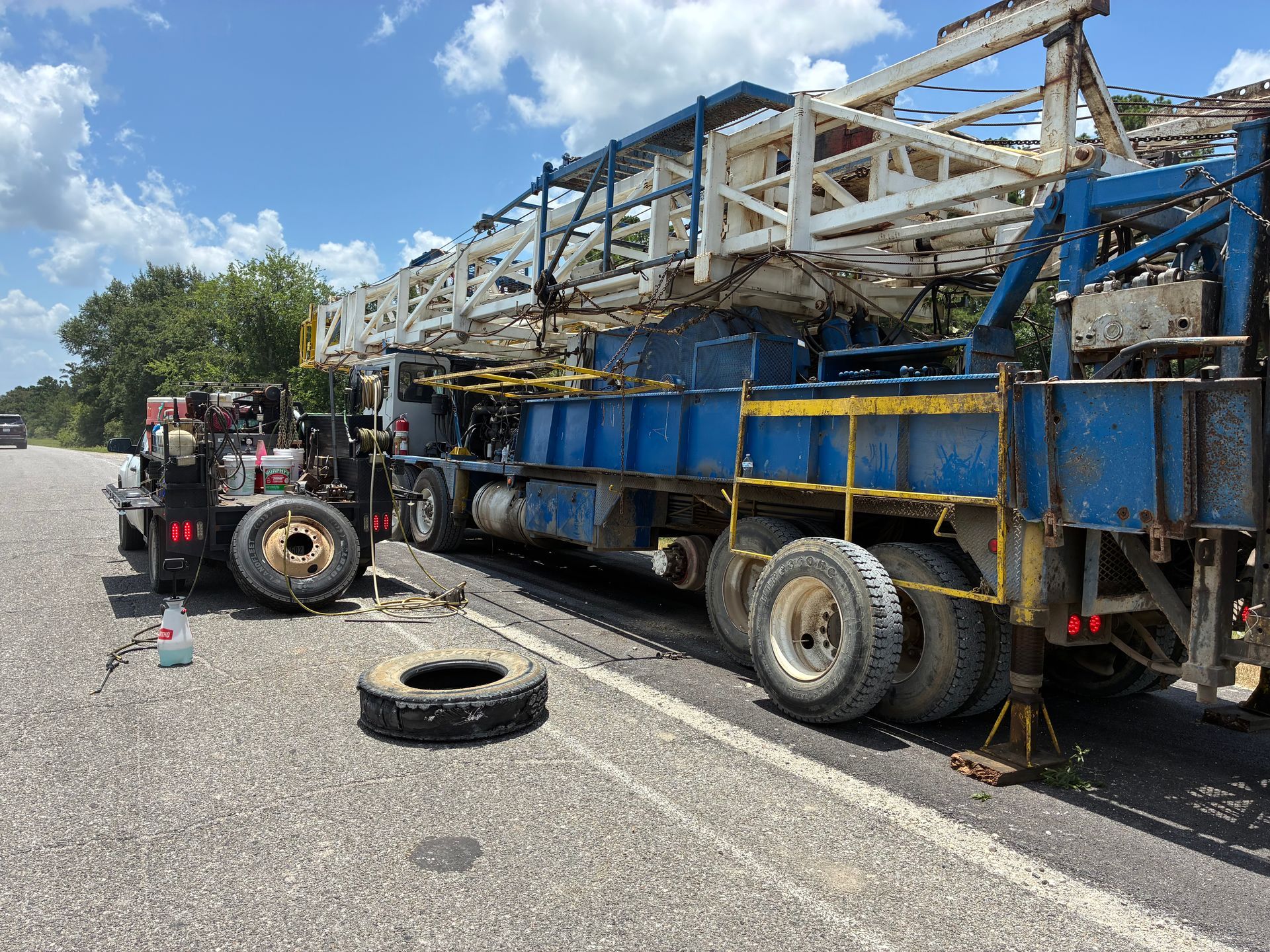 Forklift beside a blue flatbed truck carrying a damaged white metal structure on a roadside.