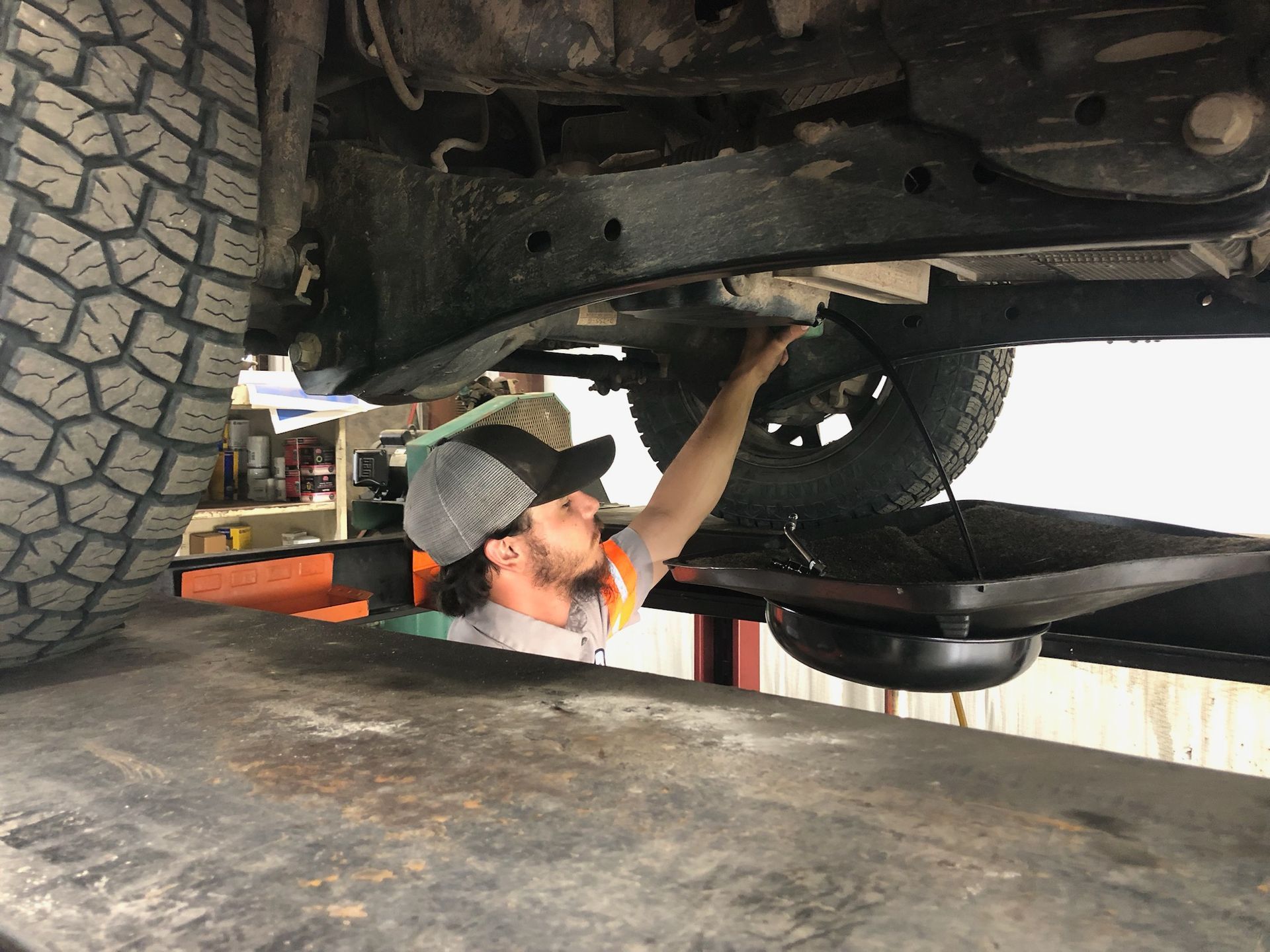 Mechanic under a truck, changing oil in a shop.