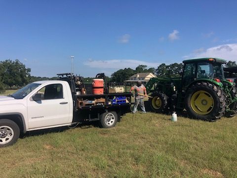White truck and green tractor on grassy field. A man stands between them. Blue sky.