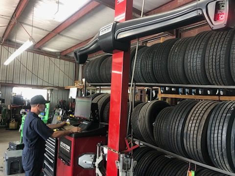 Mechanic balancing tire at a shop, surrounded by stacks of tires; indoor with a red machine.