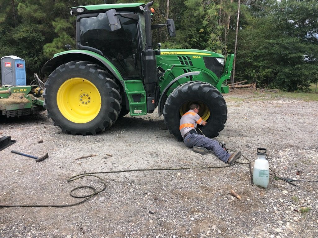 Man working on the tire of a large green and yellow tractor in a gravel area.