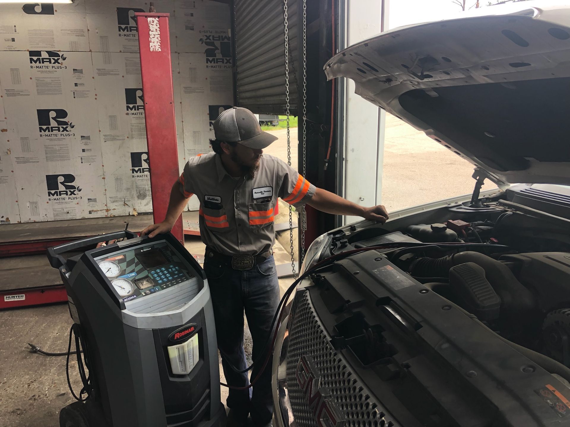 Mechanic checks car engine at auto shop. Man wearing work uniform; a diagnostic machine is near.