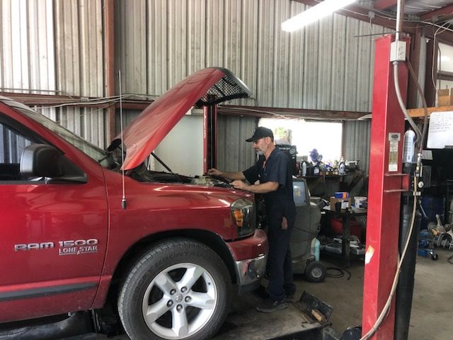 Mechanic in a shop works on a red Ram 1500 truck with the hood open.