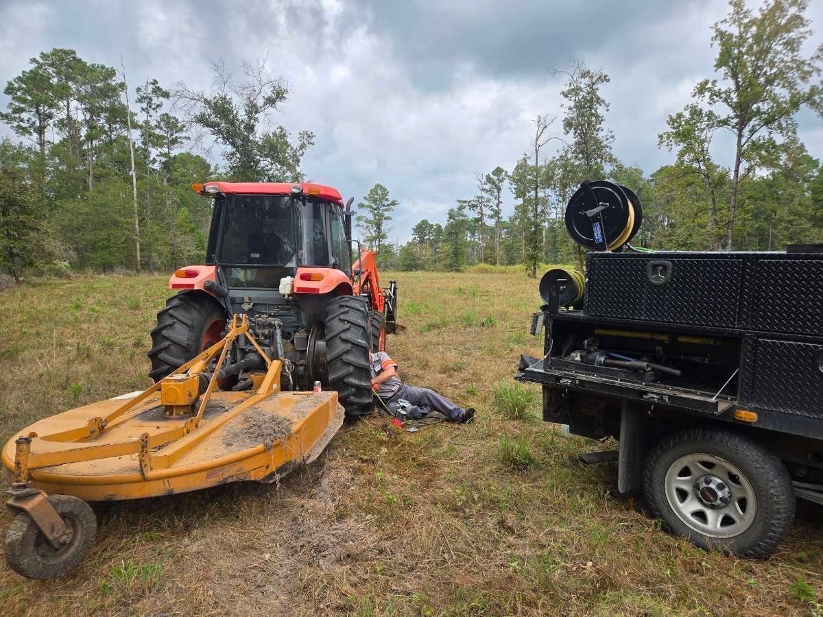 Orange tractor with mower, person down on ground, next to a black utility truck.