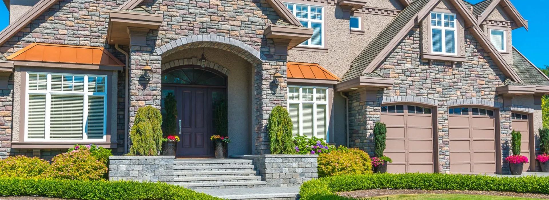 A large brick house with two garages and a lush green yard.