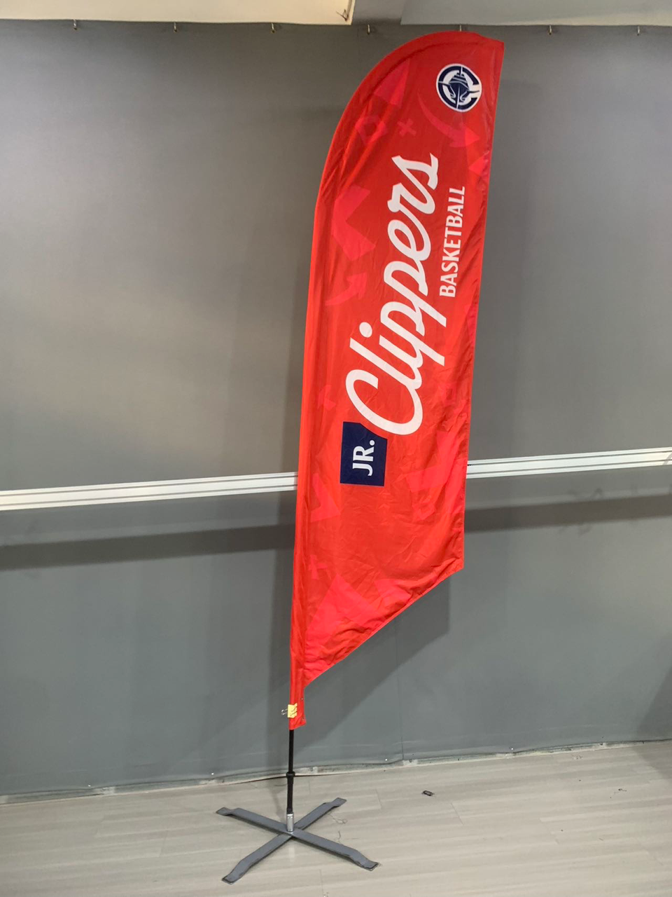 Red Clippers flag with logo on a stand in front of a gray wall.