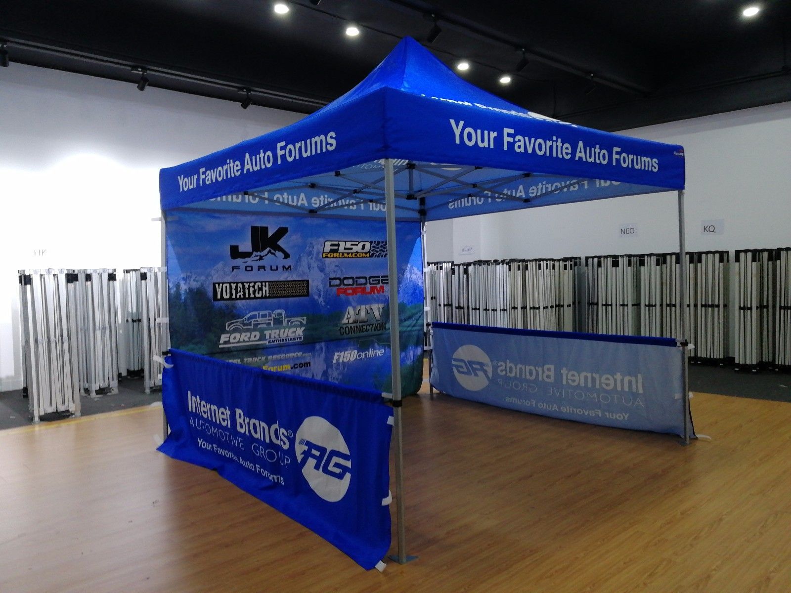 Blue pop-up tent with logos for auto forums on display at an event.