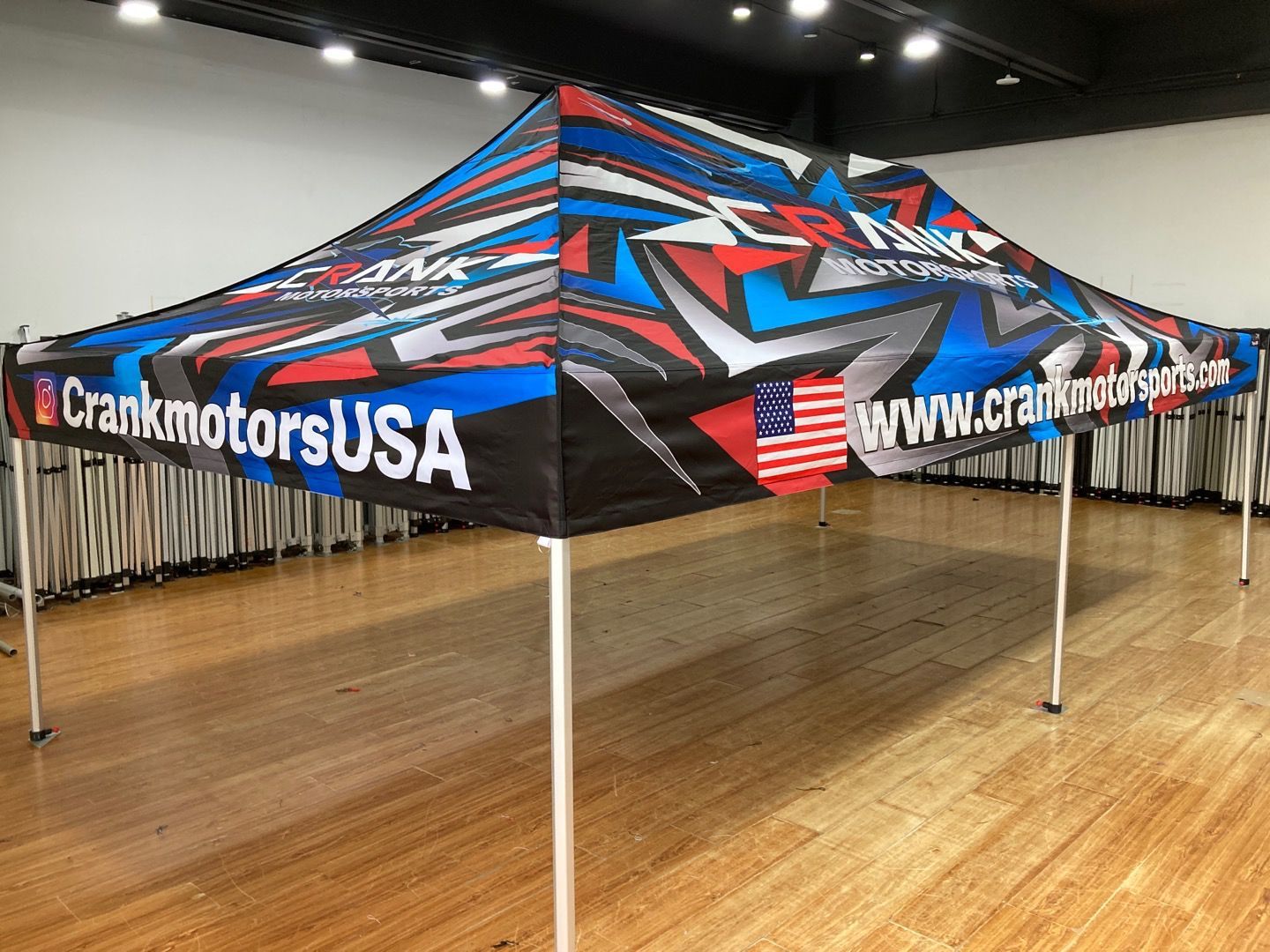 A Crank Motors USA branded event tent, with a red, blue, and gray design, set on a wood floor.