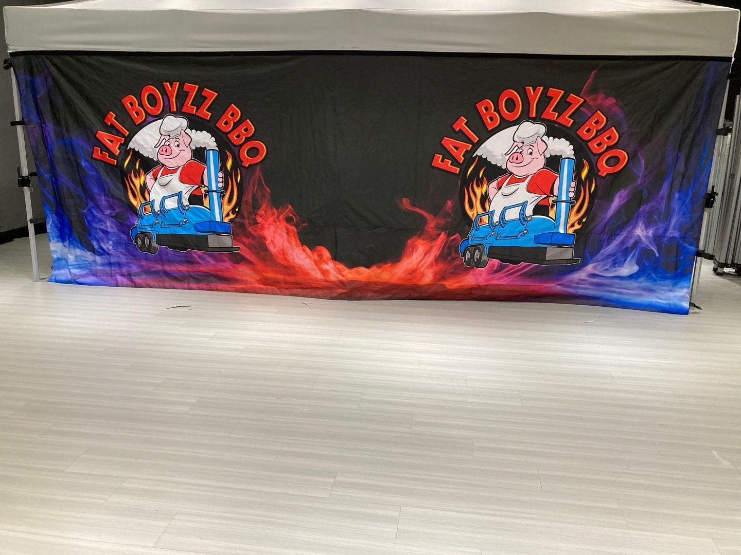 Fat Boyzz BBQ tent with logo, colorful smoky background.