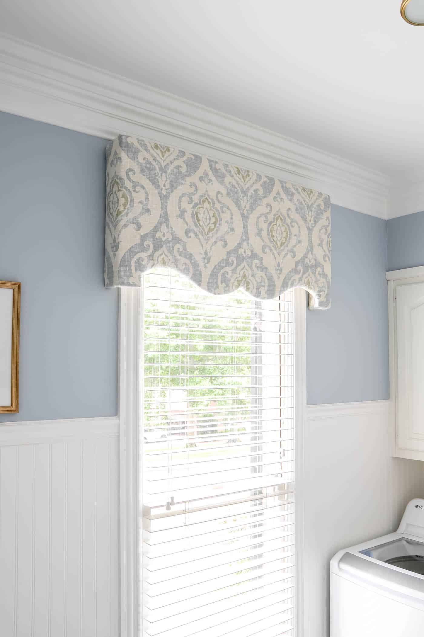 Blue and white patterned valance above a window with white blinds, light blue wall.