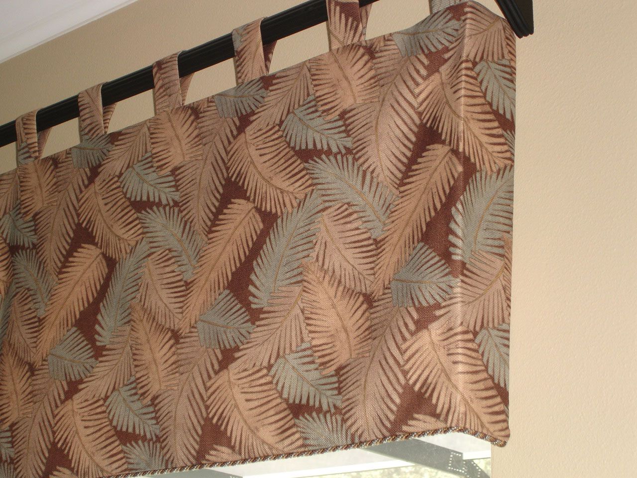 Brown and tan leaf-patterned valance with loops, hanging above a window.