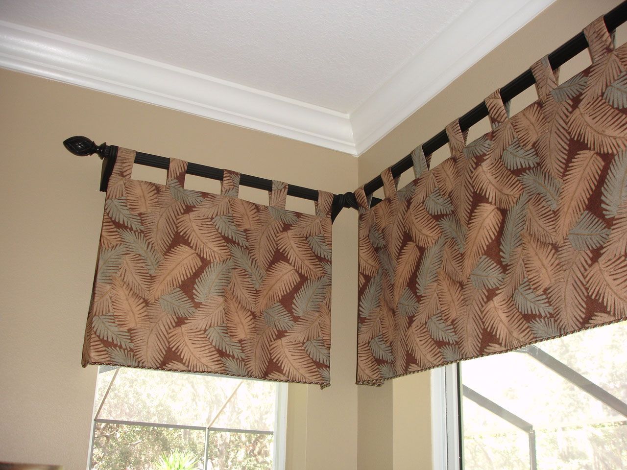 Brown and tan patterned valance on black rods over a corner window.