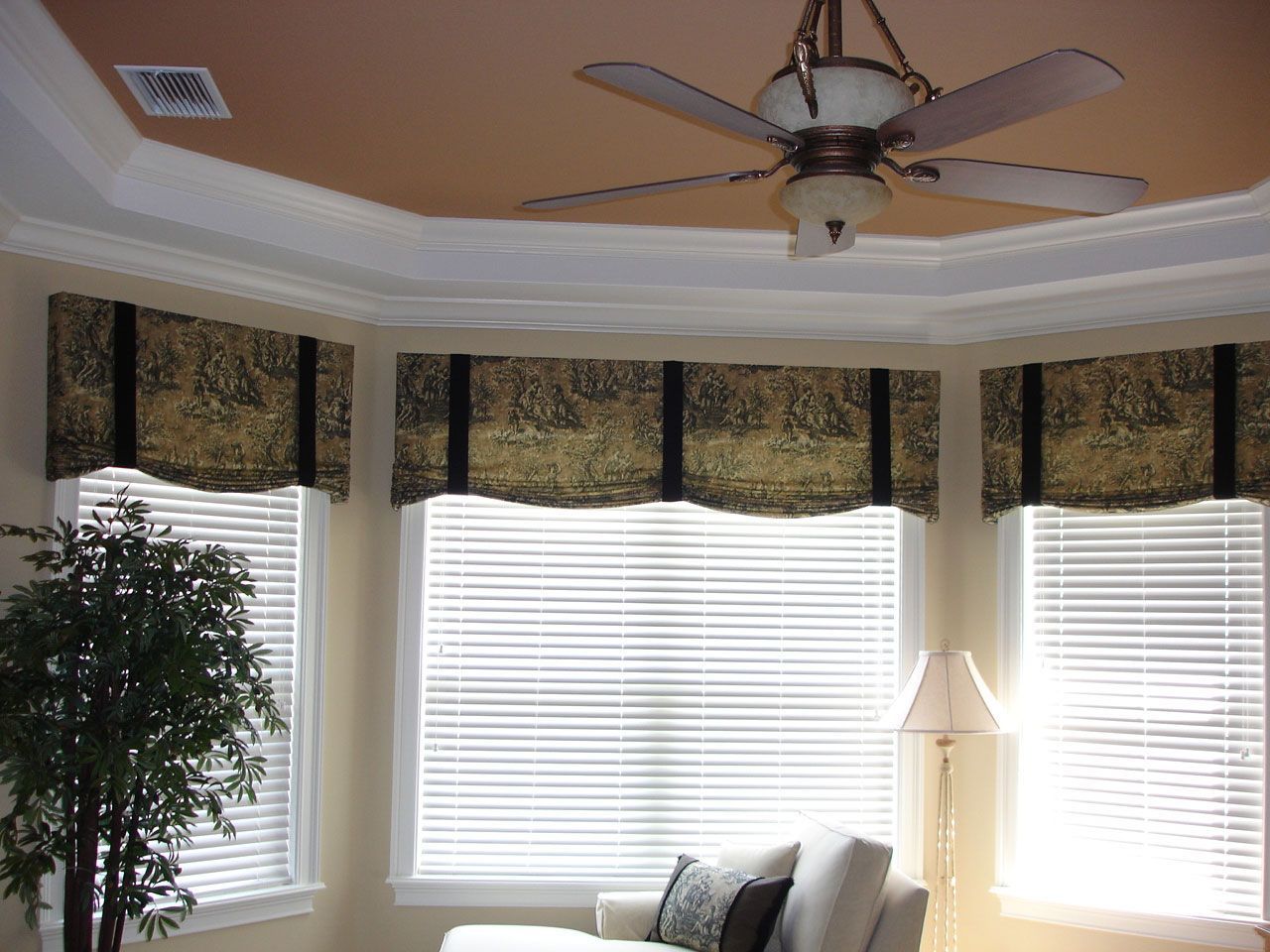 Living room with three windows, patterned valances, and ceiling fan. Includes blinds and a white sofa.