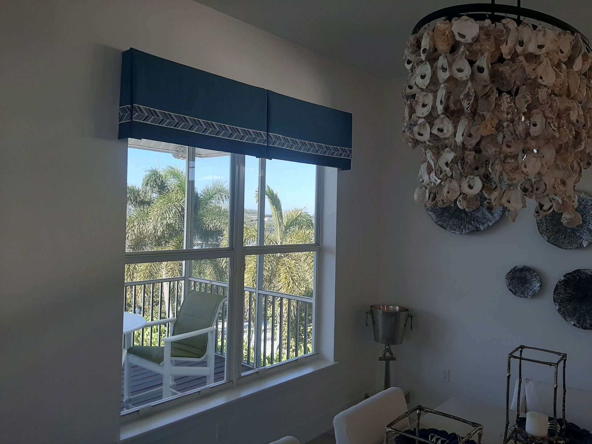 Blue valance above a window with outdoor view; chandelier and dining area to the right.