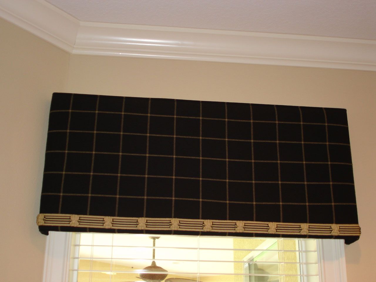 Black and gold grid valance above a window with beige walls and white trim.