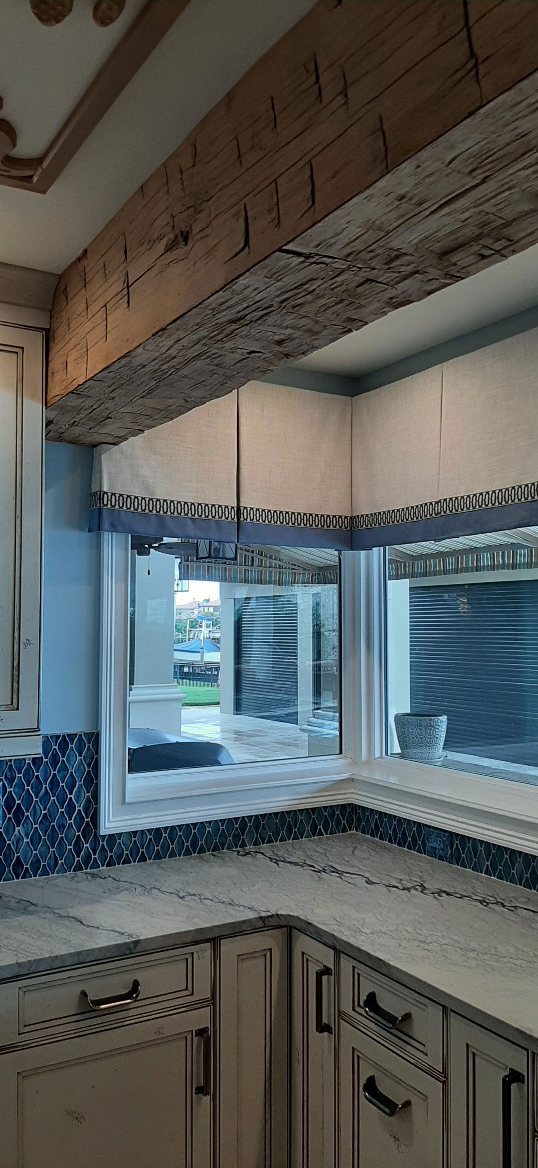 Kitchen with light-colored cabinets, wood beam ceiling, and a window looking outside.