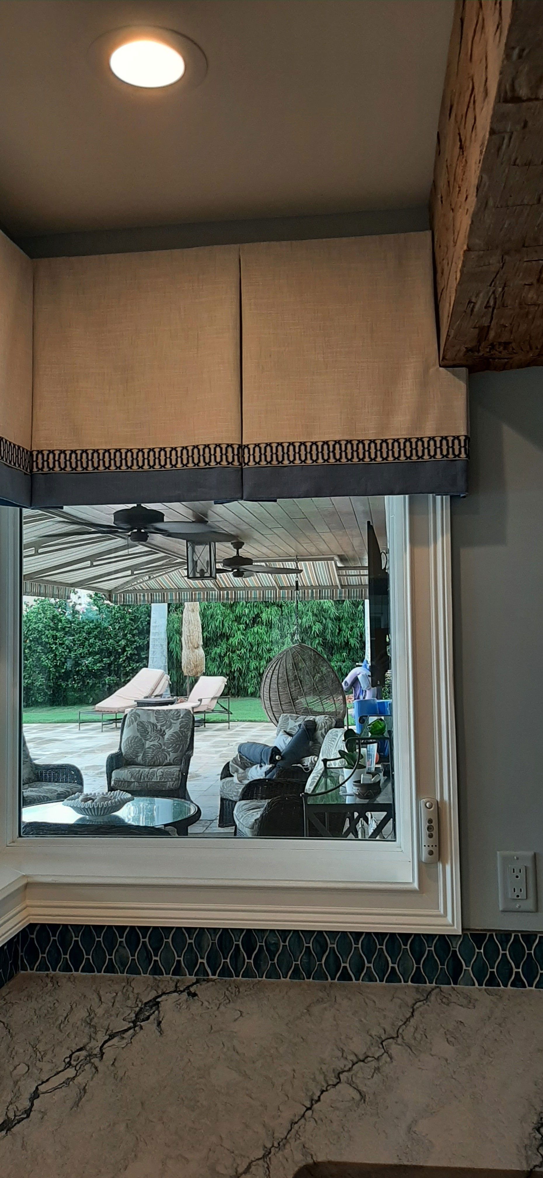 A kitchen window with a view of a patio, curtains, and a granite countertop.