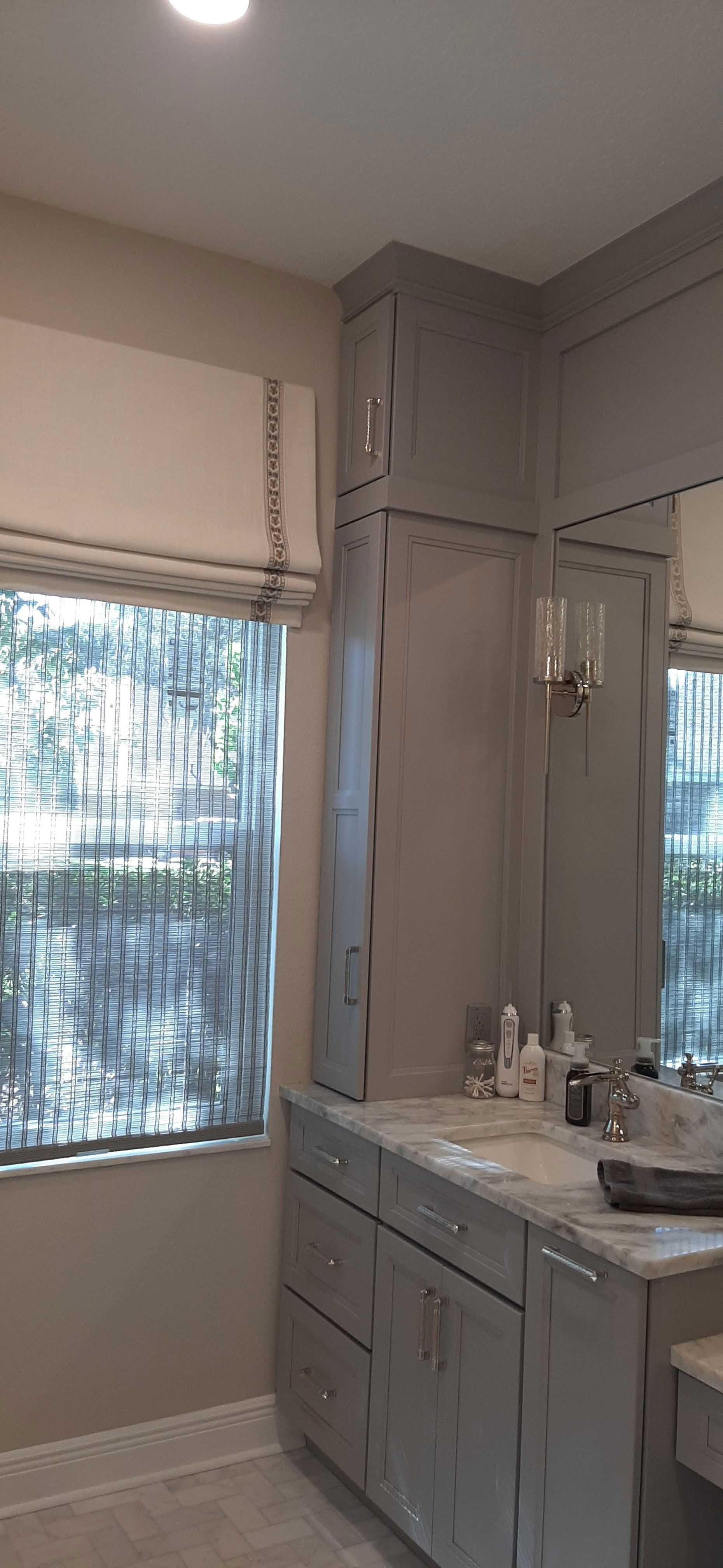 A light grey bathroom vanity with matching cabinets and a window with a white shade.