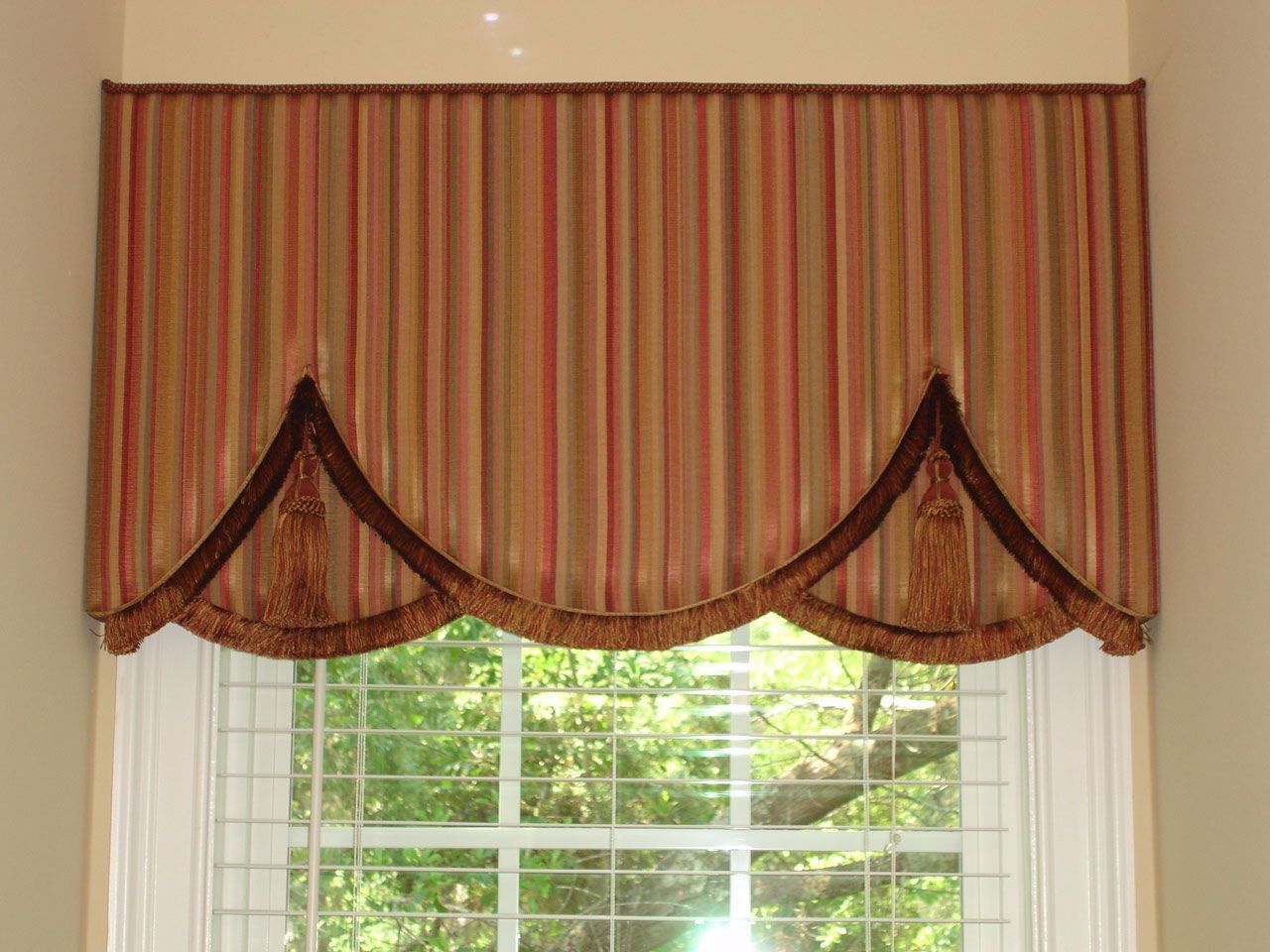Striped valance over a window, with brown accents and decorative fringe.