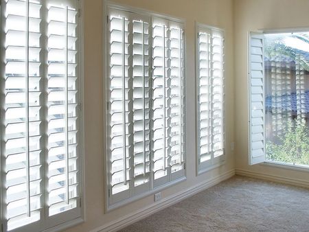 A room with a lot of white shutters on the windows