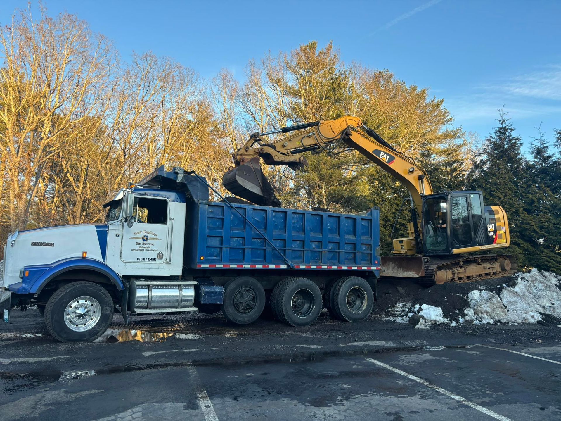 White dump truck and excavator clearing snow on a roadside under a blue sky