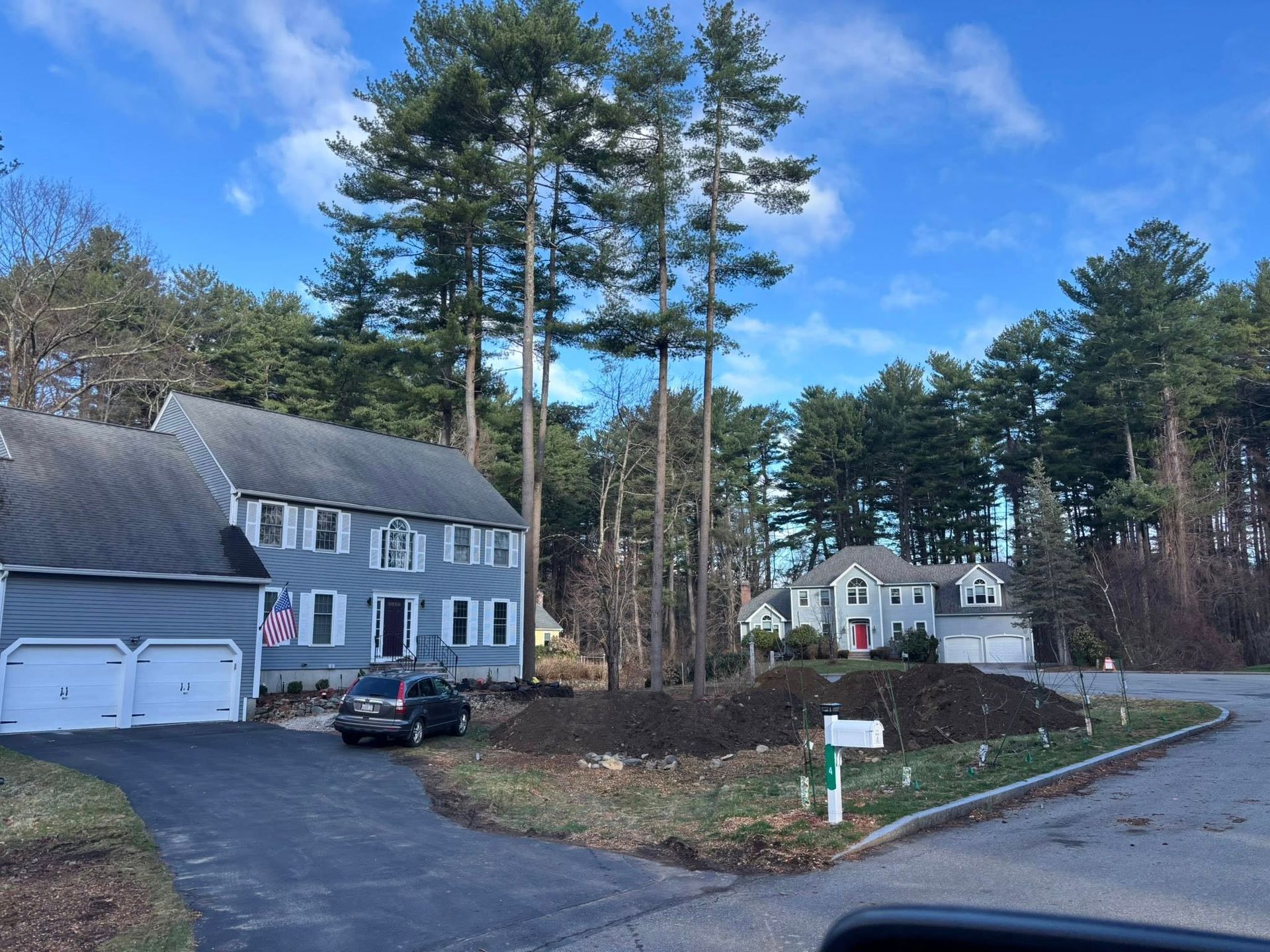 Suburban house with garage and driveway beside a wooded lot under a blue sky