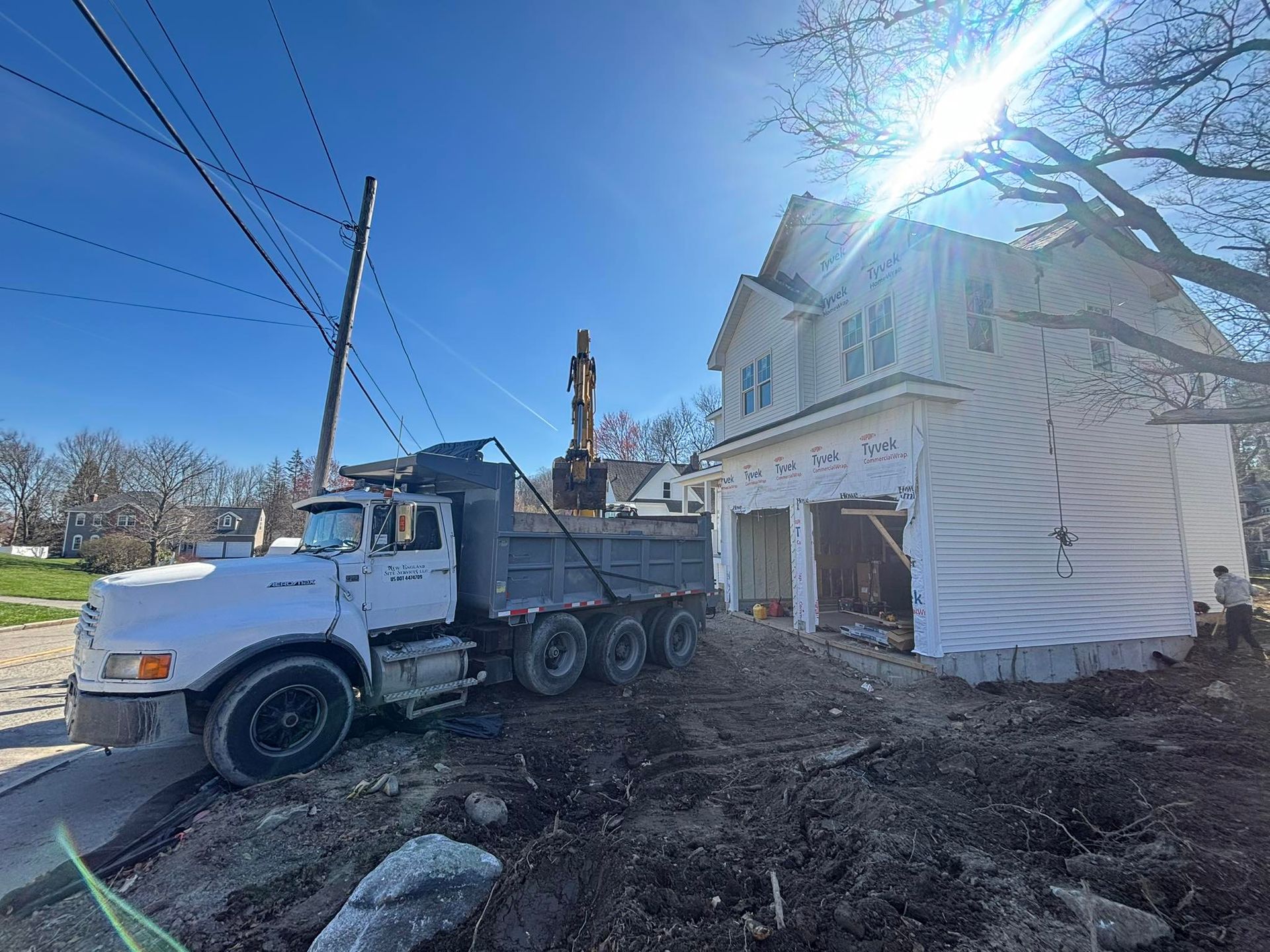White dump truck at a muddy construction site beside a house under renovation on a sunny day