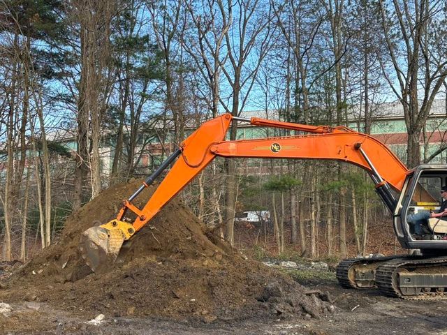 Orange excavator digging a dirt pile in a wooded area with bare trees