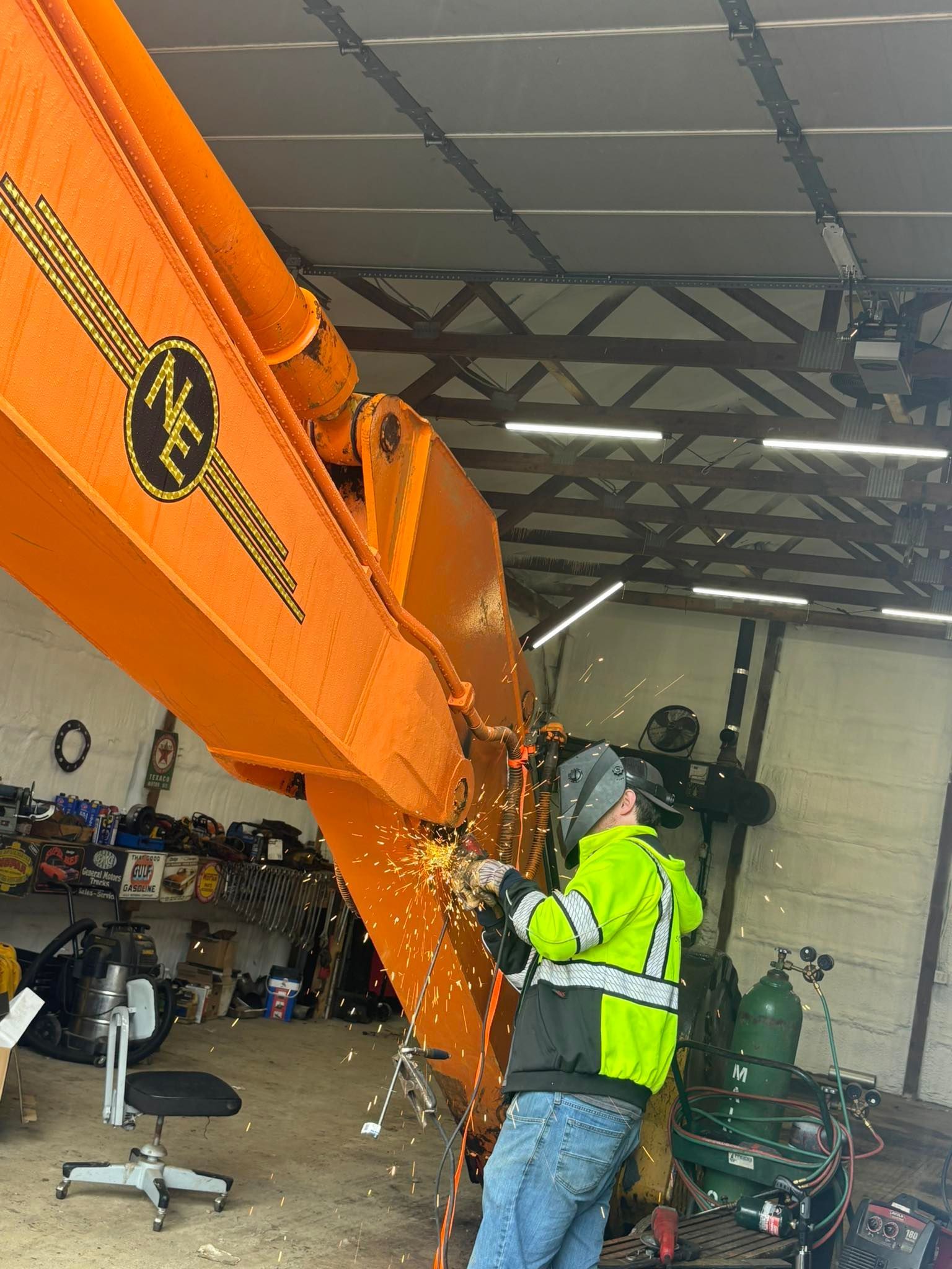 Worker in a neon vest cutting a large orange metal beam in a workshop, with sparks flying.