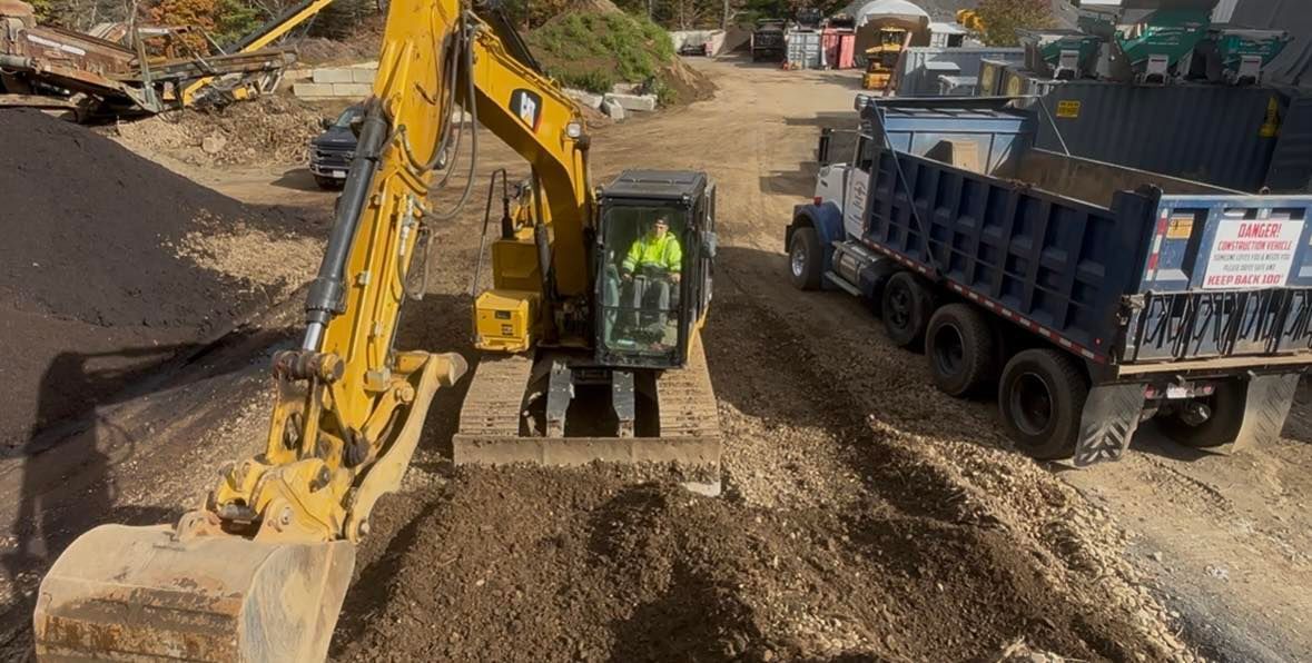 Yellow excavator loading dirt into a blue dump truck at a construction site