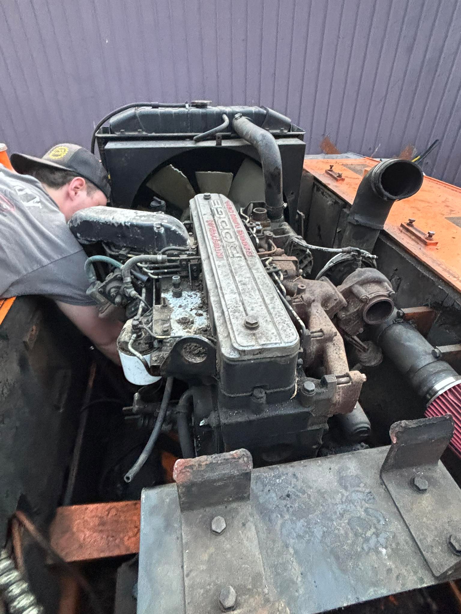 Mechanic working on a dusty engine in an orange equipment compartment outdoors