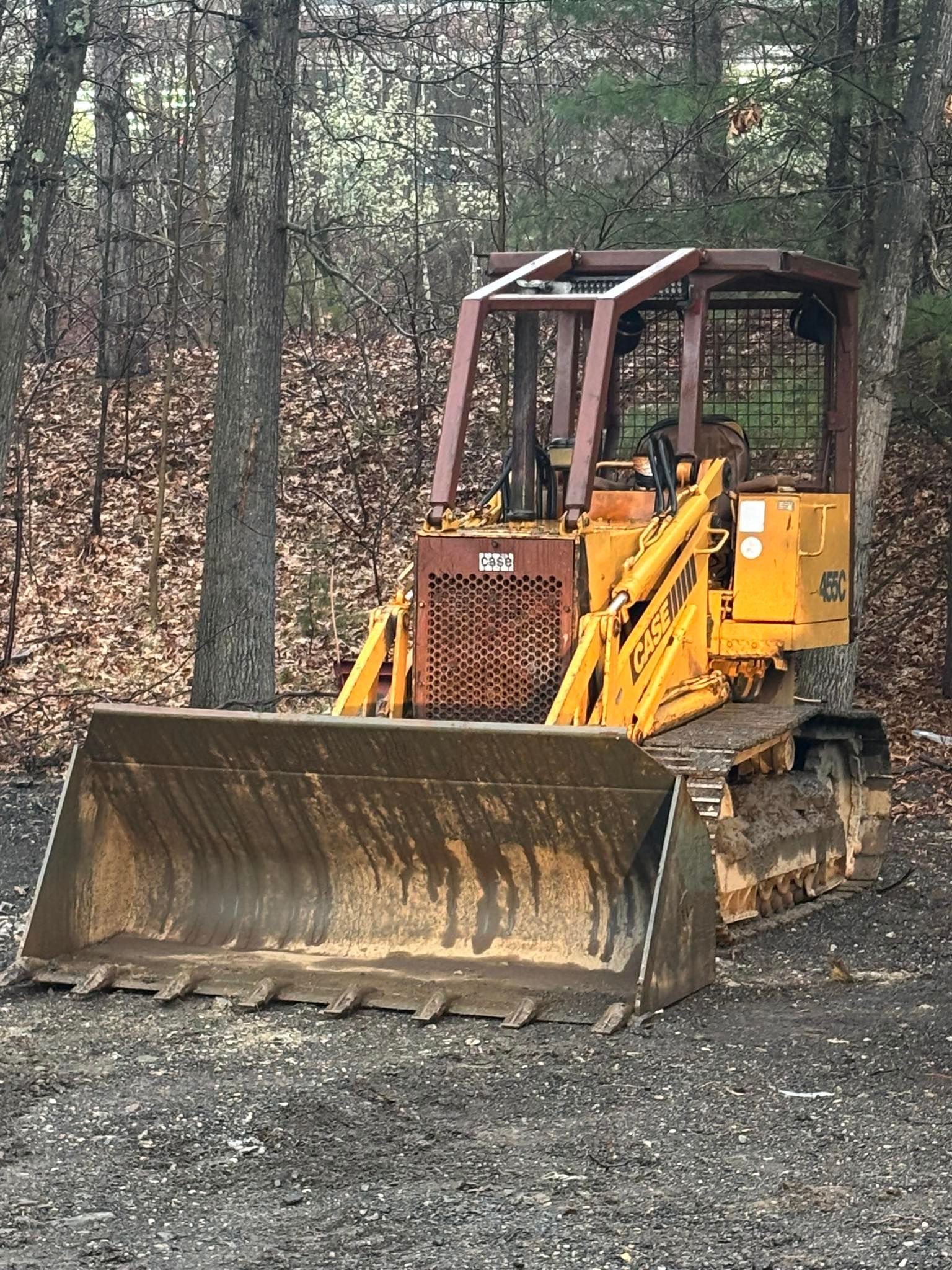 Yellow bulldozer with front blade on a muddy forest road, surrounded by bare trees.