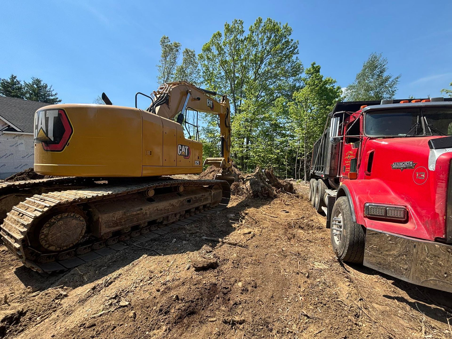 Yellow excavator beside a red dump truck on a dirt construction site with trees in the background