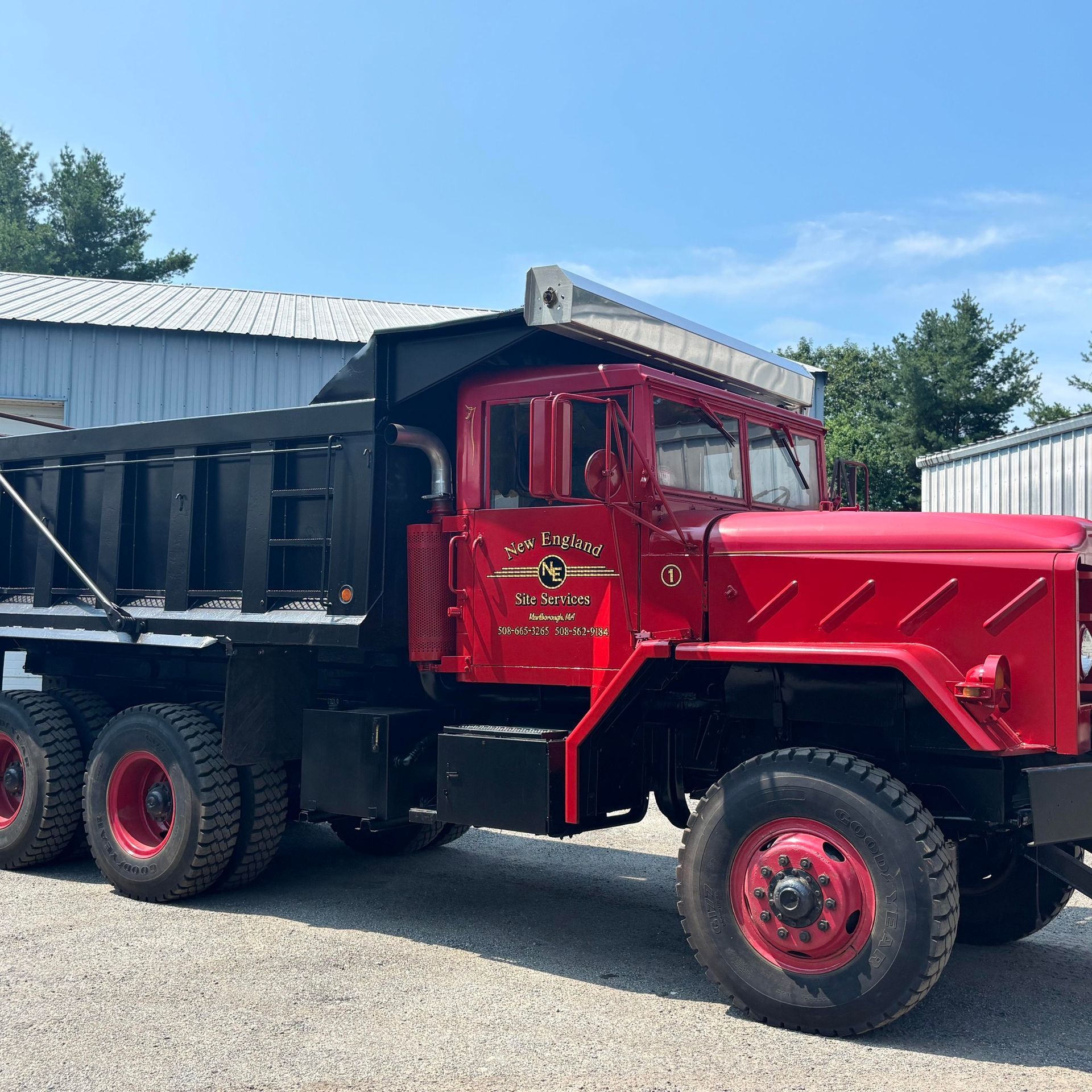 Red vintage dump truck with black bed parked outdoors on gravel under a blue sky