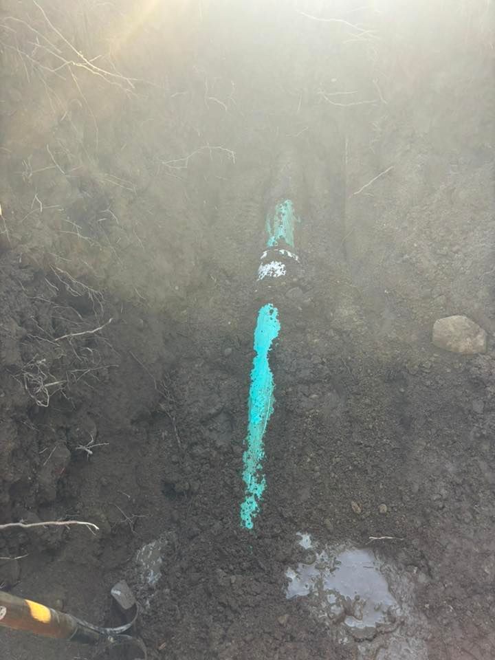 Close-up of a muddy trench with a bright blue pipe running vertically through the center.