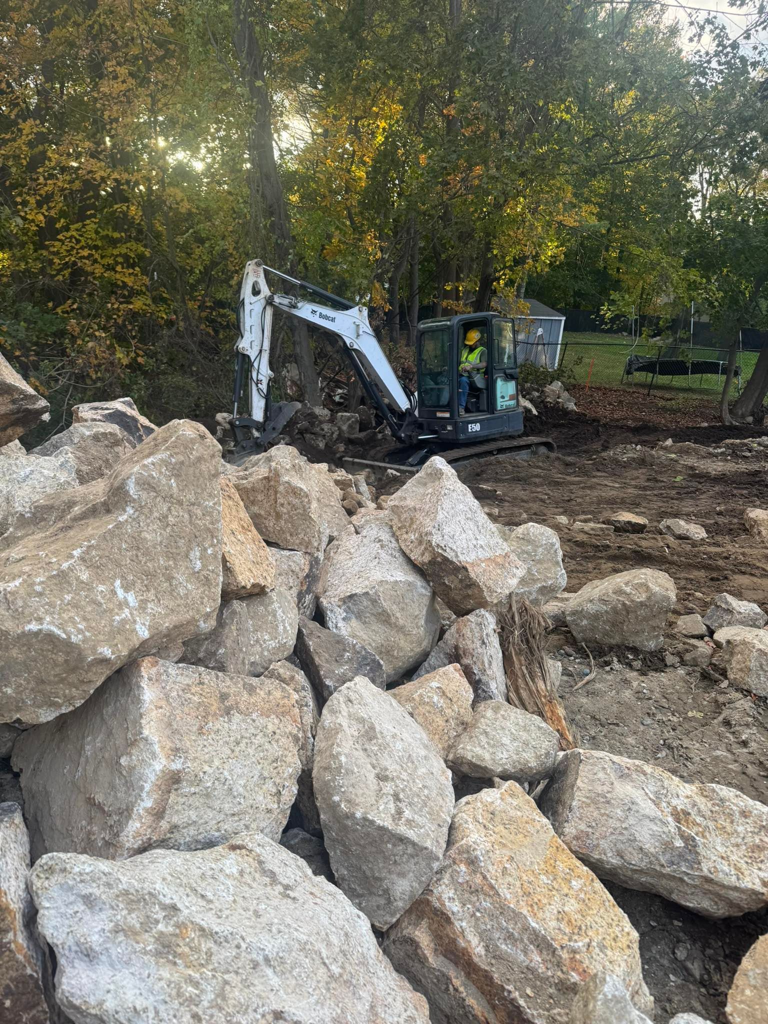 Excavator behind a pile of large boulders in a wooded construction area