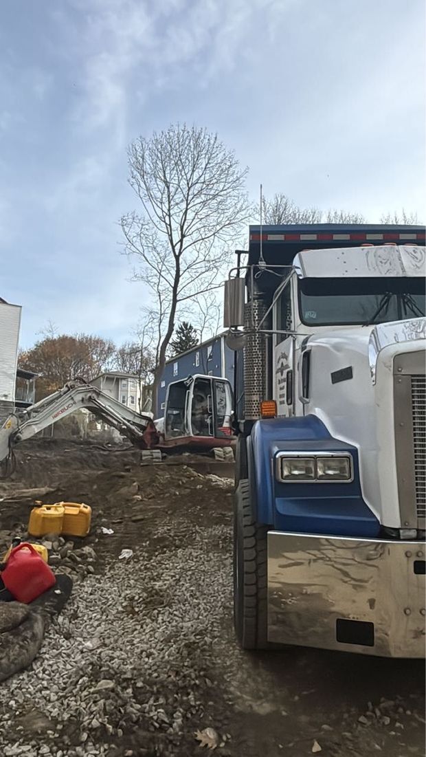 Front end of a blue-and-white dump truck at a construction site with debris and equipment nearby